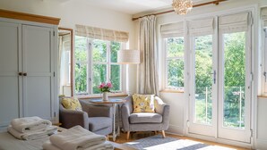 Una habitación con cama, silla, mesa y ventanas amplias con cortinas.