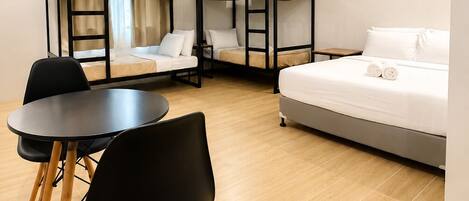 Une chambre d’hôtel avec des lits superposés, un lit simple, une table ronde avec des chaises et une fenêtre avec des rideaux.