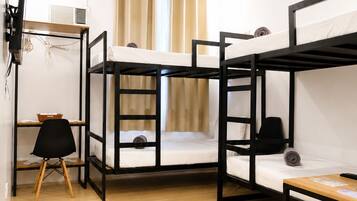 A dormitory room with bunk beds, a desk, a chair, a TV, and an air conditioning unit.