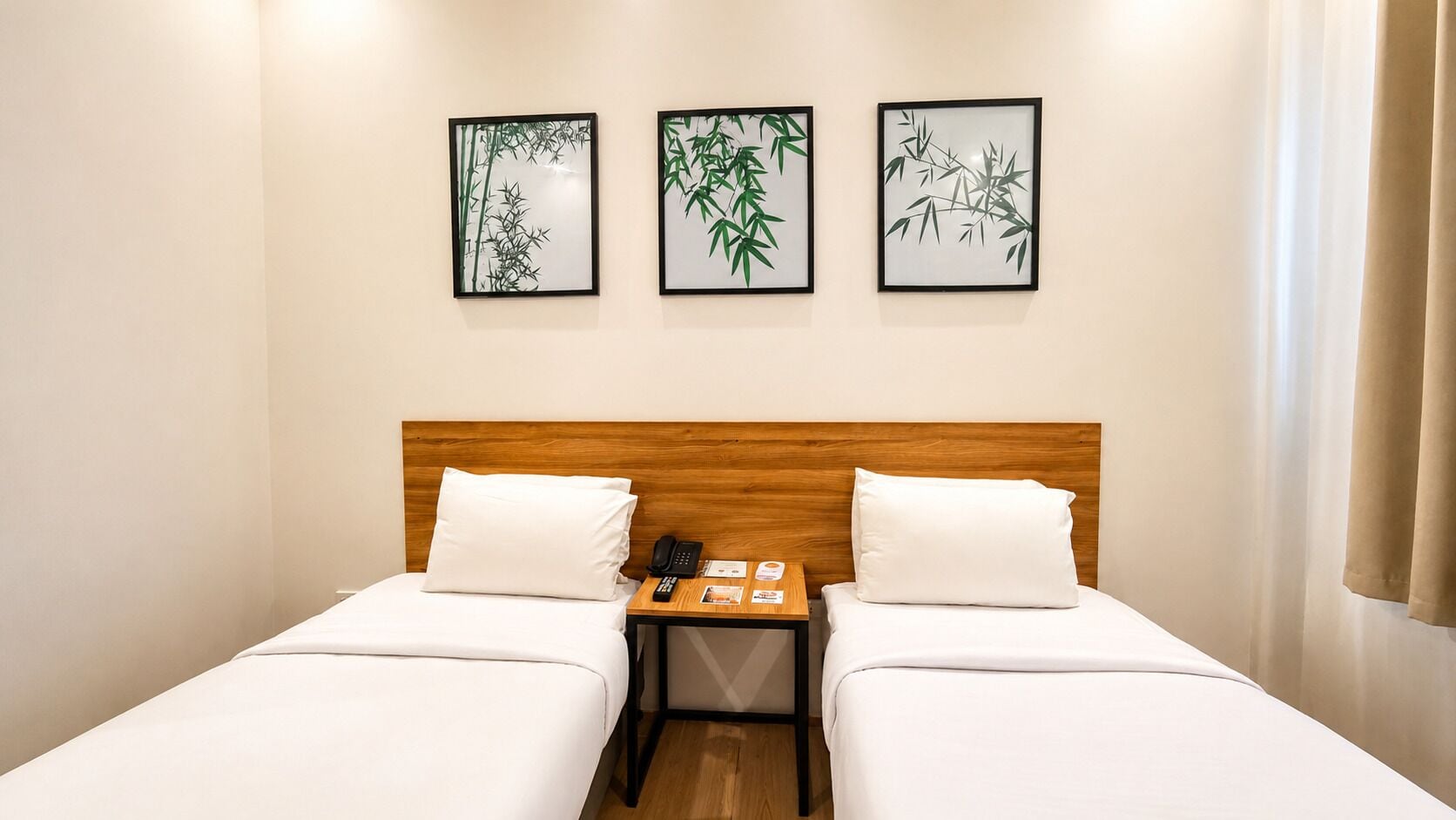 A double bed with a wooden headboard, two bedside tables with a phone and a book, and three framed bamboo artwork on the wall.