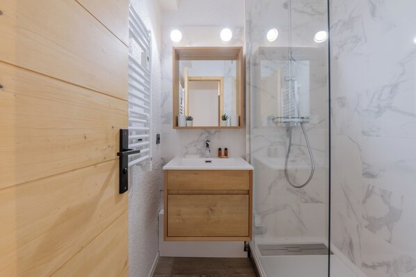 Un baño moderno con tocador de madera, cabina de ducha de vidrio y pared con azulejos de mármol.