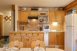 A kitchen with wooden cabinets, a microwave, a refrigerator, and a dining table set with plates and glasses. - Residence Montana 3BR Argentière Ski Base + Parking + View for 6, Argentière (Chamonix), France (Argentière (Chamonix))