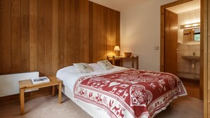 Een slaapkamer met een wand van houten panelen, een bed met een deken met een rood-wit patroon, een nachtkastje met een boek en een bedtafel met een lamp.