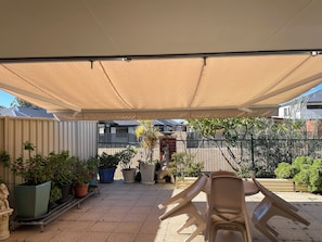 Ein überdachter Patio-Bereich mit Topfpflanzen, einer Statue und Gartenmöbeln.