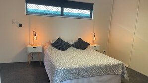 A neatly arranged bedroom with a bed, two bedside tables, and a window with blinds. - Fully Self contained 1bedroom spacious unit adjoining rear of owners home. (Jandakot)