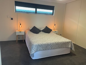 Ein ordentlich eingerichtetes Schlafzimmer mit einem Bett, zwei Nachttischen und einem Fenster mit Jalousien.