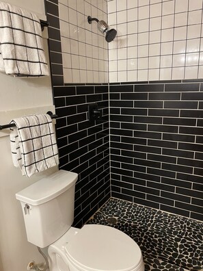 A bathroom with a toilet, a shower, and black and white tiled walls.
