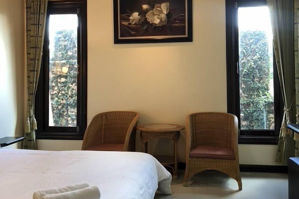 Habitación de hotel con una cama grande, dos sillas de mimbre, una mesita y un cuadro en la pared.
