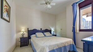 A bedroom with a bed, nightstands, a ceiling fan, a window with curtains, and a wall-mounted picture.