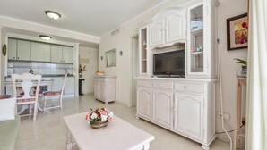 A spacious living area with a dining table, white cabinetry, a flat-screen TV, and a flower vase.