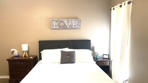 Una cama bien hecha con sábanas blancas, un cabecero oscuro y un letrero en la pared que dice "LOVE".