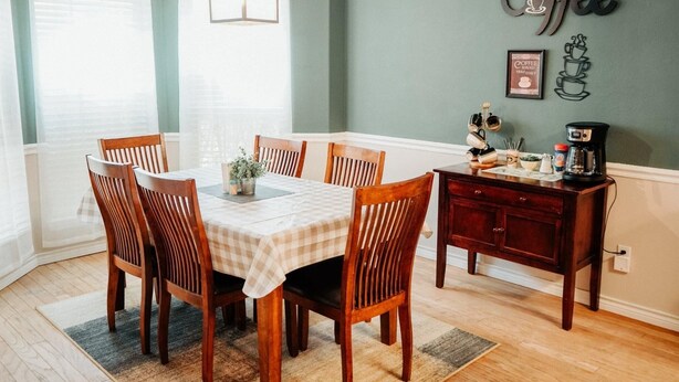 Un comedor con una mesa preparada para seis, sillas de madera, una estación de café y un letrero en la pared que dice 