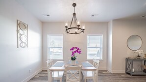 A dining area with a chandelier, white chairs, a table with a vase of flowers, and a console table with decorative items.