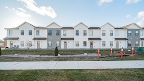 A row of modern multi-story residential buildings with a uniform architectural style, featuring a flat roof and a symmetrical facade.