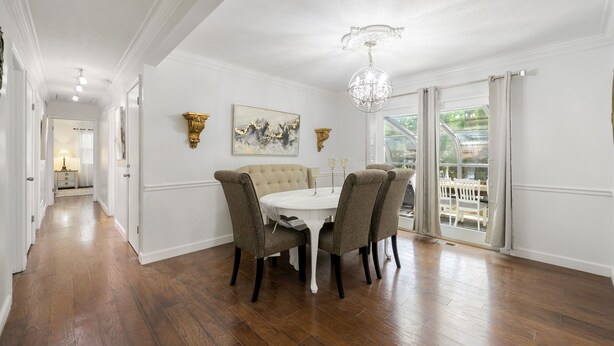 A dining area with a white table and four chairs, a chandelier, and artwork on the walls.