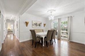 Un coin repas avec une table blanche et quatre chaises, un lustre et des œuvres d’art accrochées aux murs.