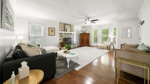 A spacious living room with a fireplace, a ceiling fan, and a large window.
