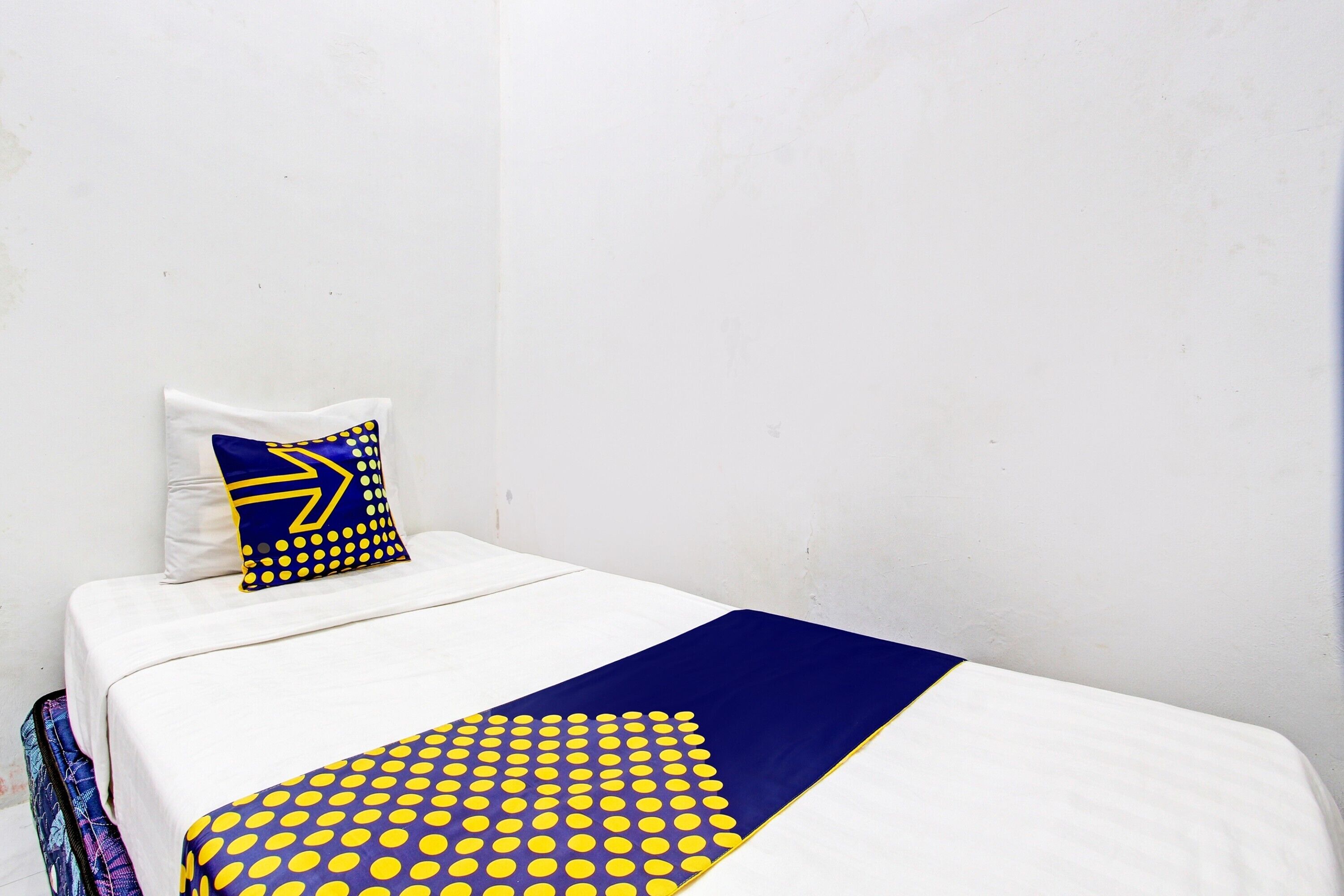 Een eenpersoonsbed met een witte matras, een deken met blauwe en gele stippen, en een kussen met een blauw-geel ontwerp.