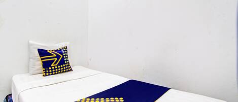 Een eenpersoonsbed met een witte matras, een deken met blauwe en gele stippen, en een kussen met een blauw-geel ontwerp.