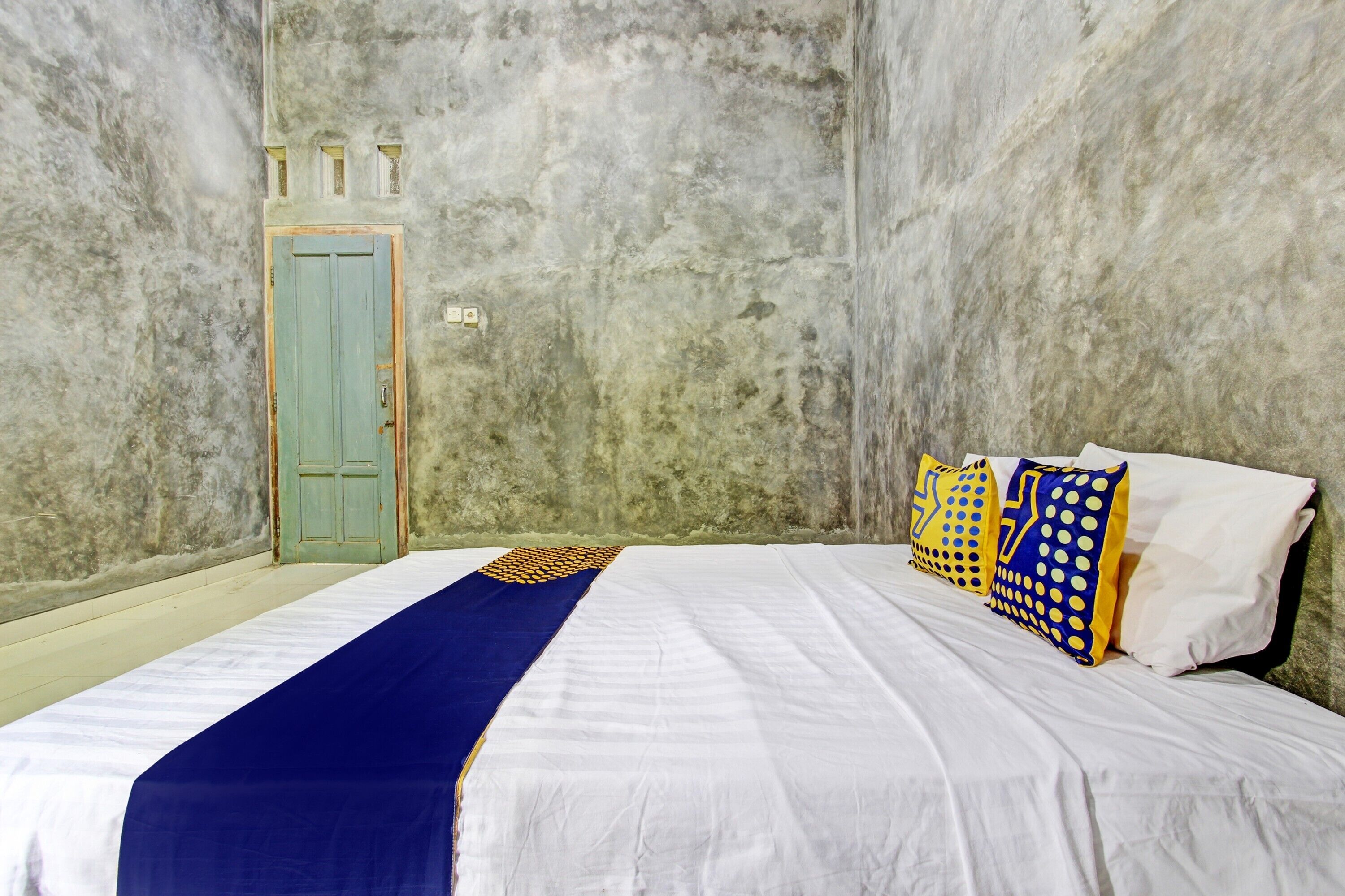 A room with a bed, a green door, and a textured wall.