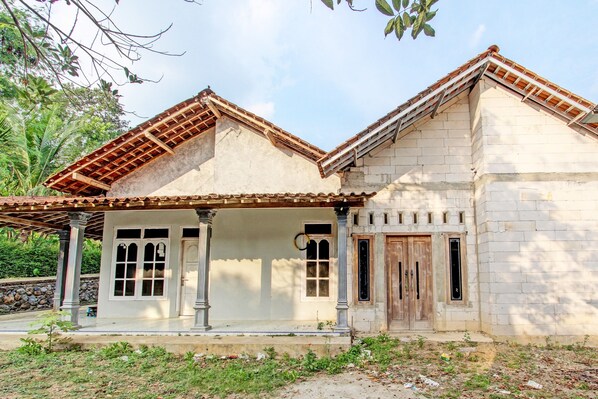 A two-story building with a tiled roof, a porch with columns, and a stone wall. - Hotel O Agus Kostel SyariahNearWisata Agro Jollong (Pati)