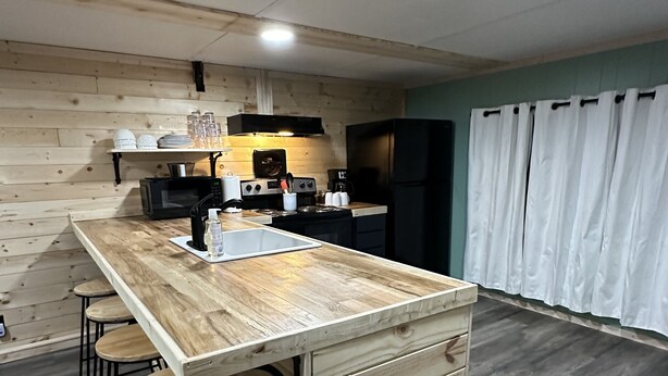 Een keuken met een houten kookeiland, barstoelen, een magnetron, een koffiezetapparaat en een koelkast.