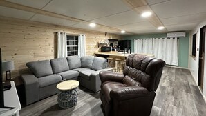 Een moderne woonkamer met een grijze modulaire bank, een bruine leren fauteuil en een klein, rond salontafel.