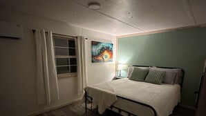 Een slaapkamer met een enkel bed, een raam met gordijnen, een aan de muur hangend schilderij en een bedlampje.