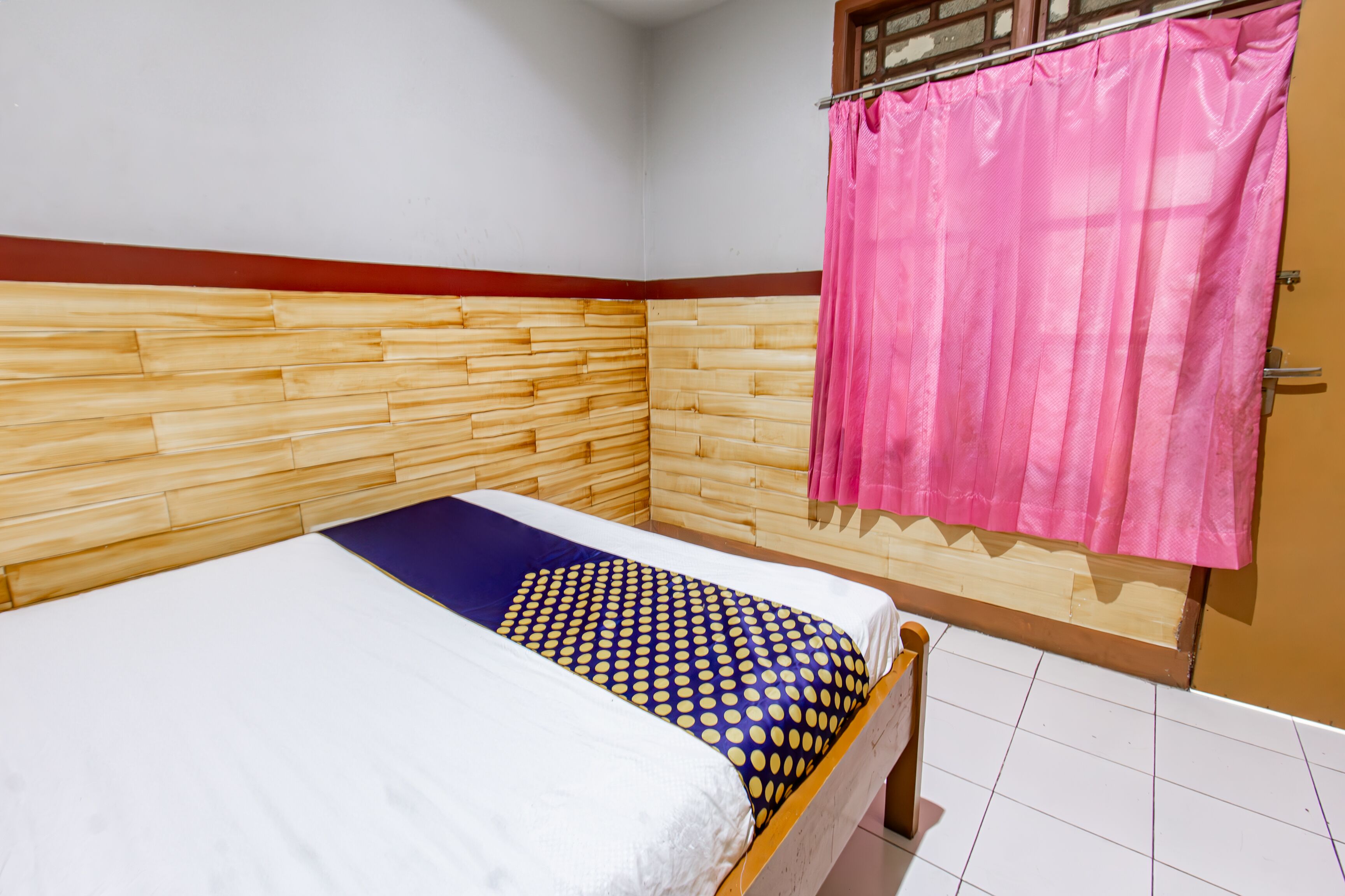 Una cama individual con cabecera de madera, cortina rosa y edredón estampado.