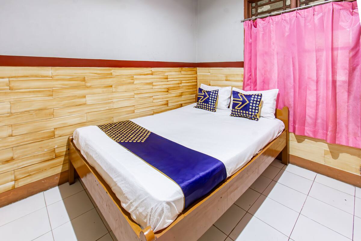 A wooden bed with white and blue bedding, pink curtains, and a wooden headboard.