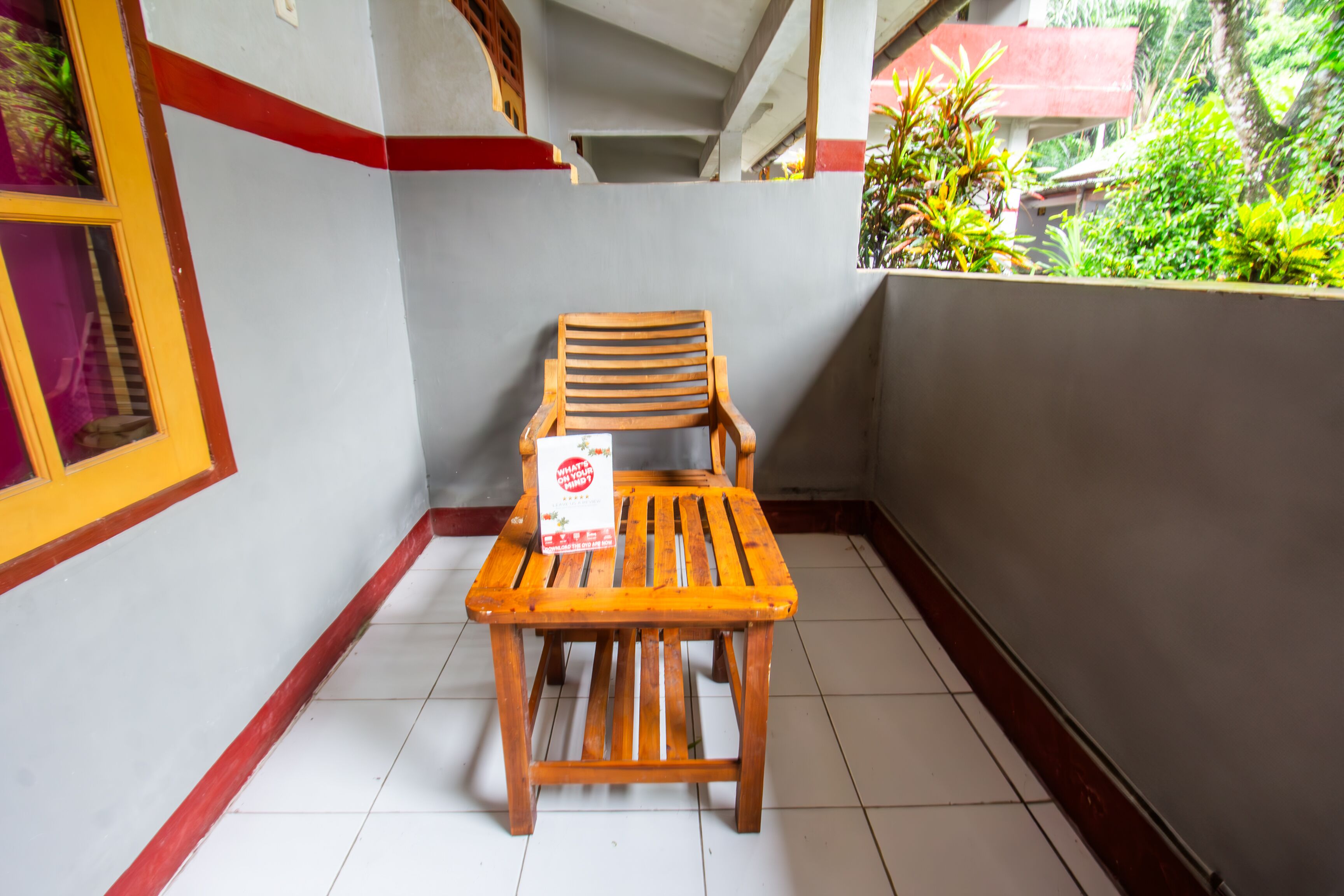 A wooden chair and table on a balcony with a tiled floor, surrounded by walls with a red trim.