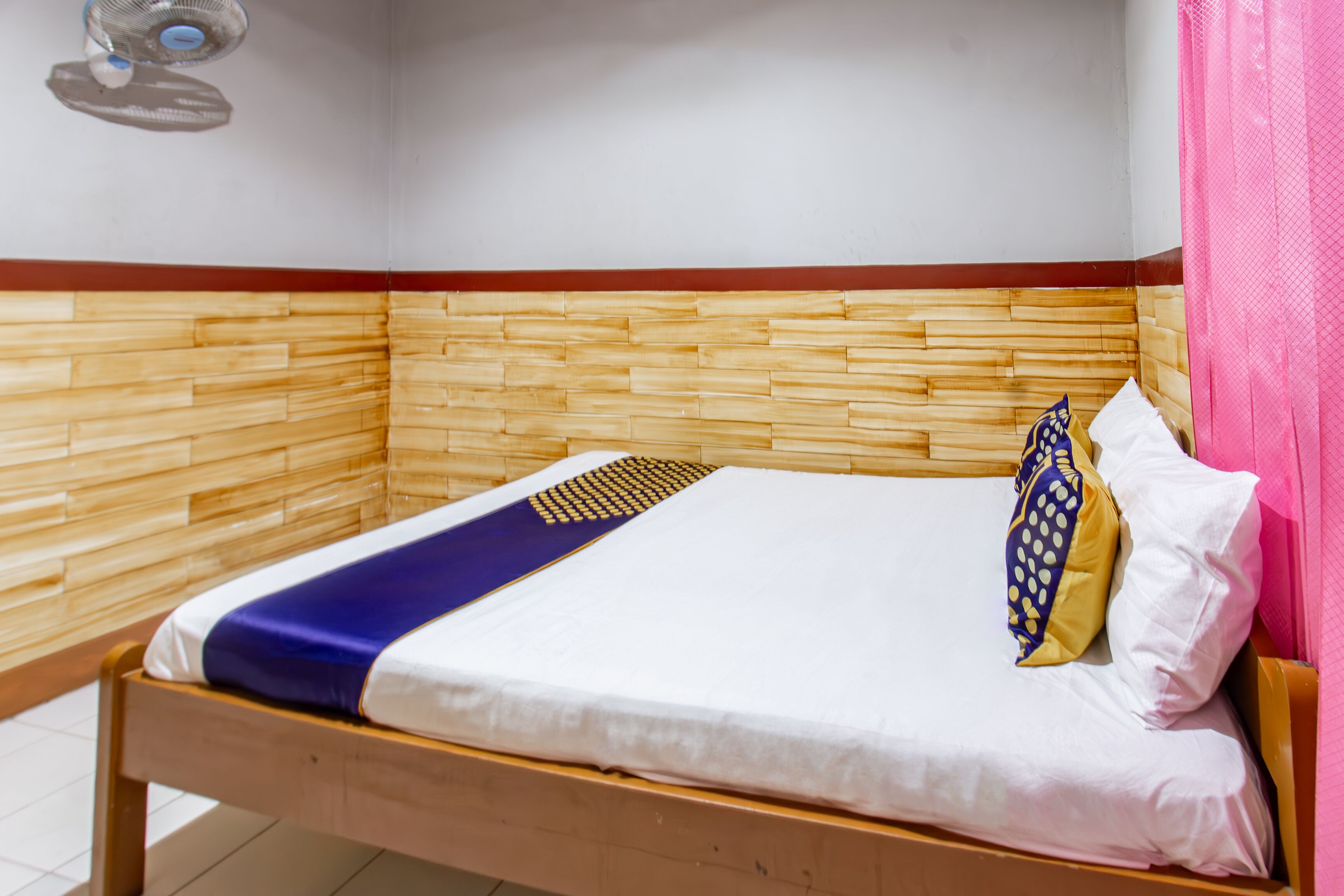 A single bed with a wooden headboard, white bedding, and a blue and yellow pillow.