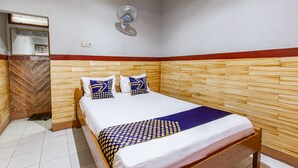 A hotel room with a wooden headboard, a bed with white and patterned bedding, a mirror, and a wall-mounted fan. - Hotel O De Lanang Homestay Near Masjid Janapria (Janapria)