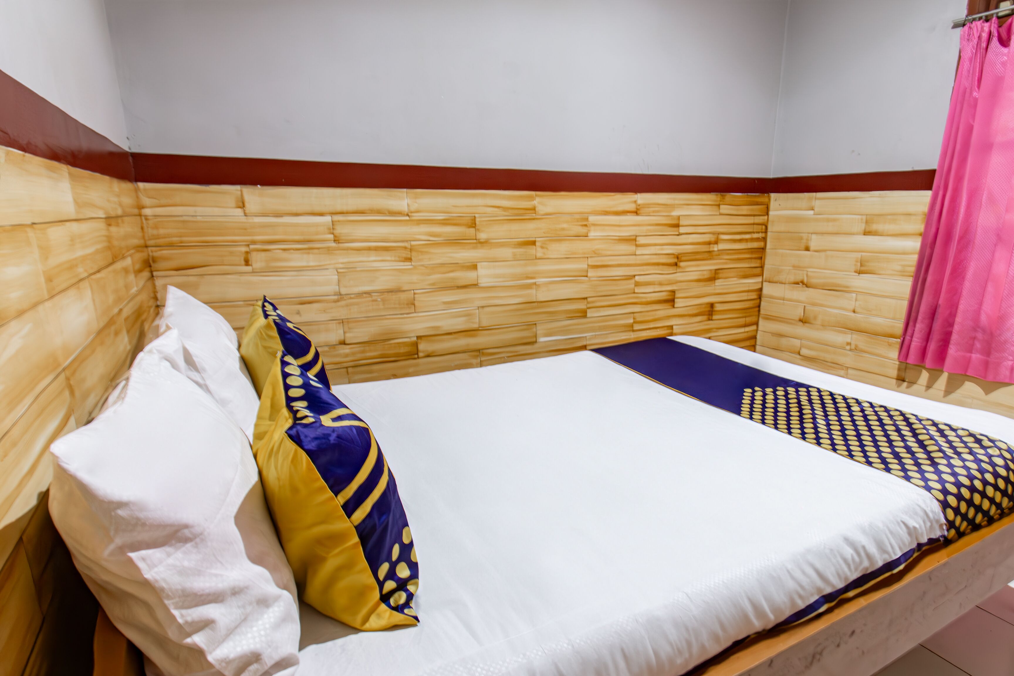 A single bed with a wooden headboard, white bedding, and patterned pillows.