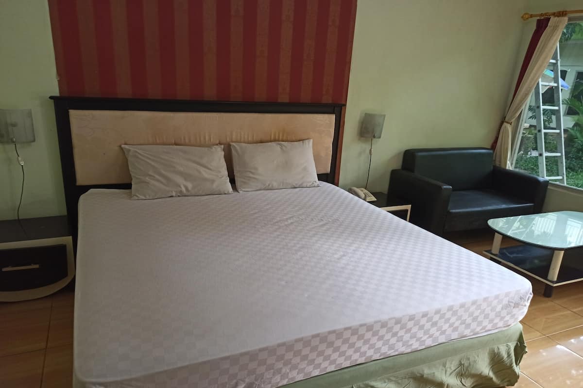 A hotel room with a large bed, a chair, a small table, and a window with curtains.