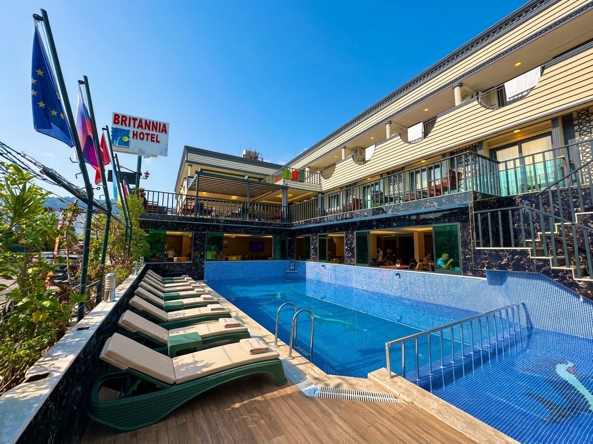Ein Poolbereich mit Liegestühlen, einem Schild für Britannia Hotel und Flaggen.