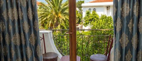 A balcony with two chairs and a table, overlooking a white building and green trees.