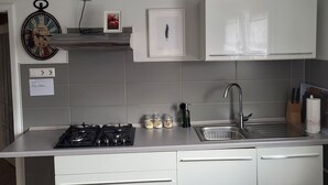 Een moderne keuken met een gasfornuis, een roestvrijstalen spoelbak, witte kasten en een klok aan de muur.
