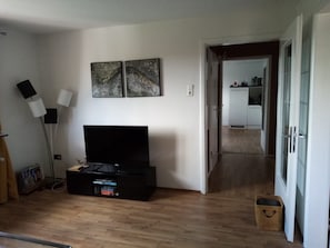 Un soggiorno con una TV a schermo piatto, una libreria e un corridoio che conduce a una cucina.
