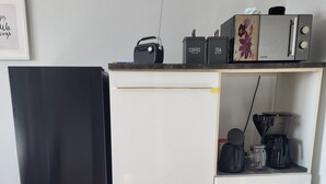Een kleine keuken met een zwarte koelkast, een witte koelkast, een koffiezetapparaat en een waterkoker op het aanrecht.