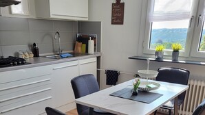 Een moderne keuken met witte kasten, een eettafel met stoelen en uitzicht op groen via een raam.