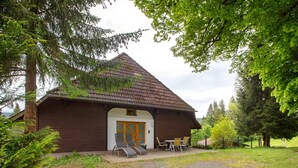 Een houten chalet met schuin dak, een voordeur en een terras met buitenmeubels.