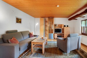 Un salon comprenant un canapé, un fauteuil, une table basse en bois et un meuble TV avec des étagères.