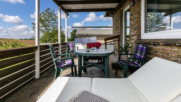 A covered outdoor area with a table and chairs, a cushioned seating area, and a view of the countryside. - Apartment 'Devich' with Private Terrace, Private Garden and Wi-Fi (Oersberg)
