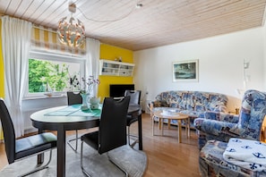 Ein Essbereich mit einem runden Tisch, Stühlen und einer Chandelüstere. Im Wohnbereich befindet sich eine Couch und ein kleiner Tisch.