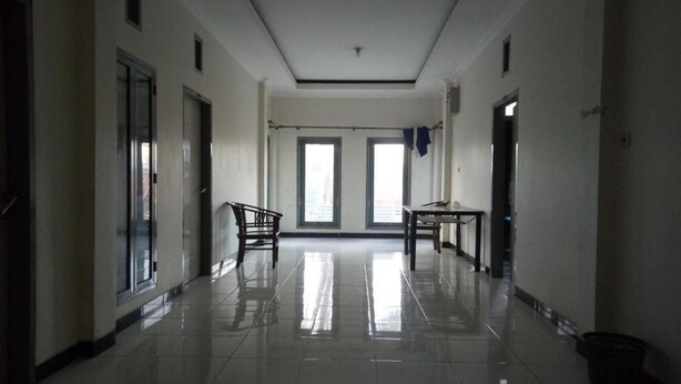 A long, narrow hallway with a tiled floor, two doors on the left, and a table and chair set on the right. - Hotel O Penginapan Kryani (Long Kali)