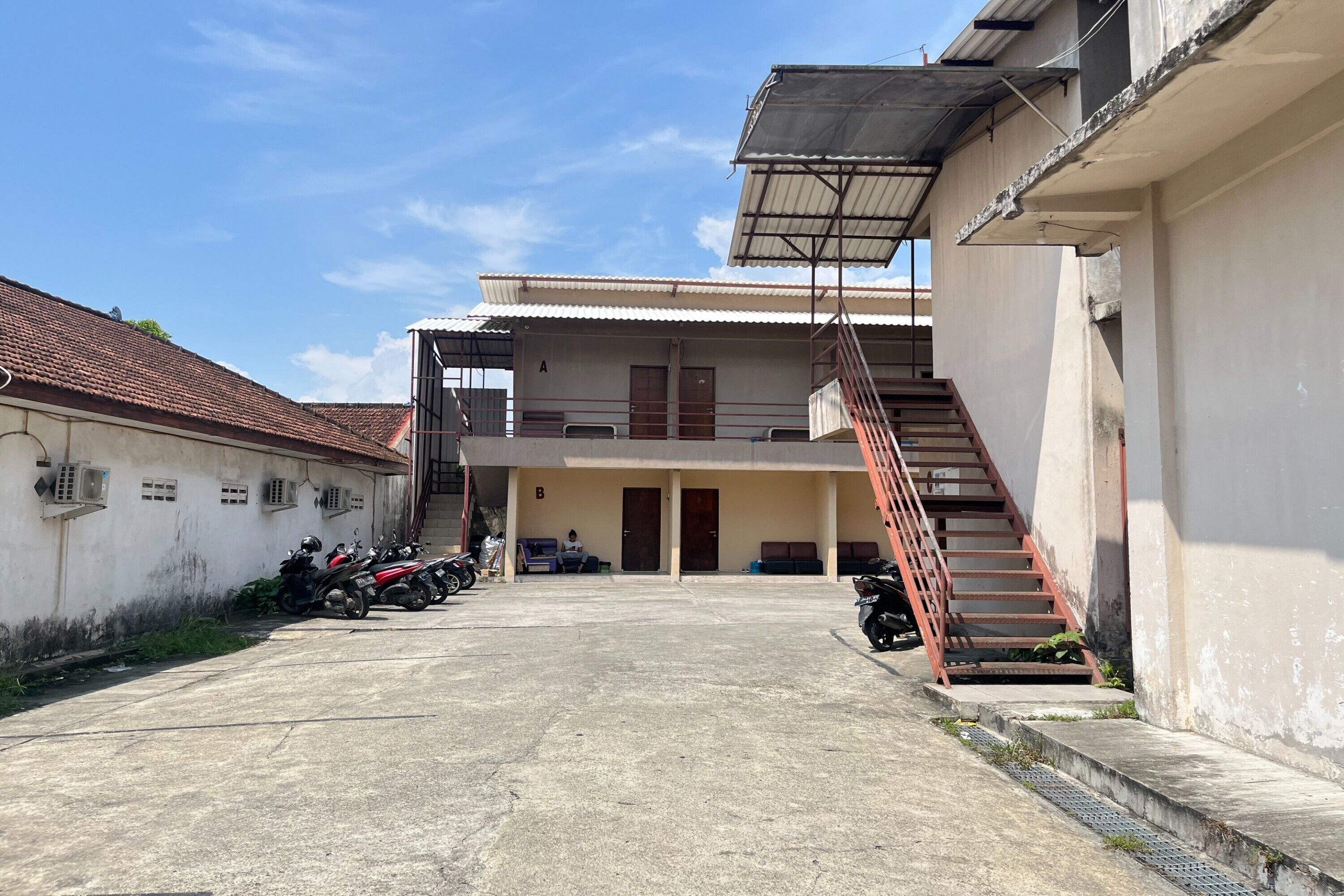 Um edifício com estrutura em dois andares, uma escadaria e uma área de estacionamento para motocicletas.