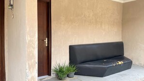 A beige wall, a wooden door, a black sofa, and two potted plants. - Hotel O Penginapan Kryani (Long Kali)