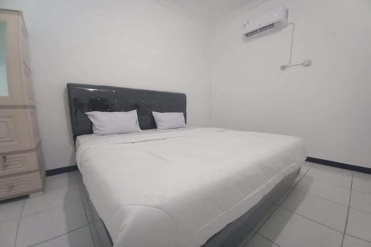 A neatly made bed with white linens in a room with white walls and a tiled floor.