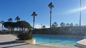 Una piscina con pavimento piastrellato, circondata da palme e da una recinzione.